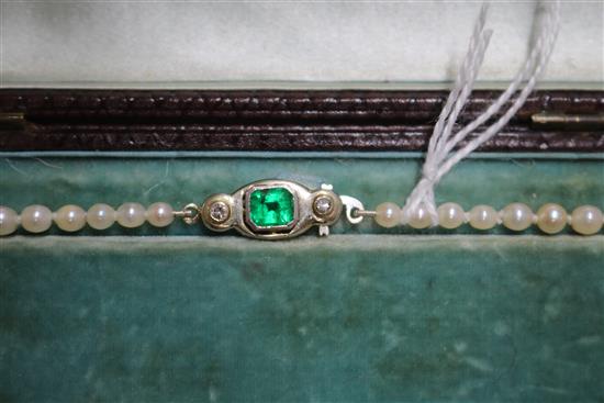 A single strand graduated cultured pearl necklace with an emerald and diamond set white metal clasp, approx. 35cm.